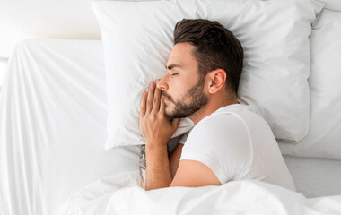 Asleep millennial man sleeping, resting peacefully in comfortable bed, lying with closed eyes, top...
