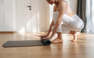 Fotobehang Rolling off the the yoga mat. Young woman in fitness clothes is in the room © standret