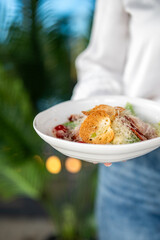Person holding a white bowl with fresh vegetable salad, featuring croutons, cheese, cherry tomatoes, and greens. Bright, natural light, blurred background, healthy meal.