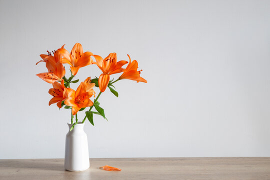 orange lilies in white vase on wooden table