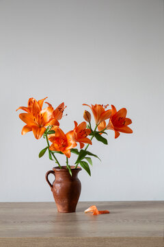 orange lilies in old clay jug on wooden table