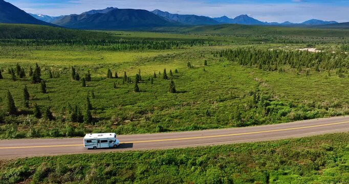 Motorhome is riding by the road in the green valley. Breath-taking mountains at backdrop. Alaska scenery.