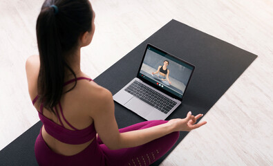 Top view of sportive young woman meditating, having yoga class online, using laptop. Unrecognizable...