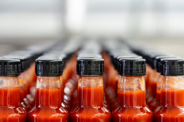 Many bottles of hot sauce waiting on conveyor belt in food processing plant