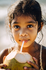 Young South Asian girl drinking coconut water with a straw on a sunny beach, close-up portrait with wet hair and natural light, perfect for travel, summer and lifestyle themes. exotic, healthy, sun
