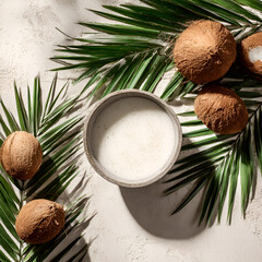Creamy coconut milk in a stone bowl surrounded by whole coconuts and palm leaves on light textured background, ideal for tropical product ads, vegan food blogs, skincare branding. exotic, natural