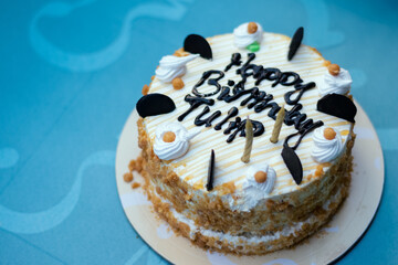Delicious birthday cake with Happy Birthday message, decorated with cream and chocolate, on a blue...