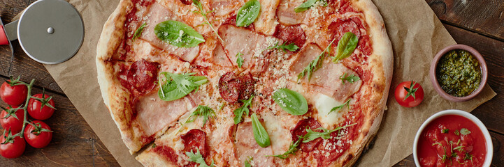 Header of freshly baked pizza with ham, pepperoni, cheese, tomato sauce, arugula and basil leaves...