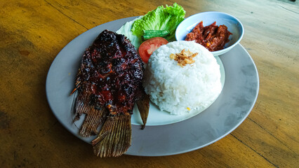 Grilled gourami salad with lettuce and tomatoes as a complement and chili sauce, on a wooden table