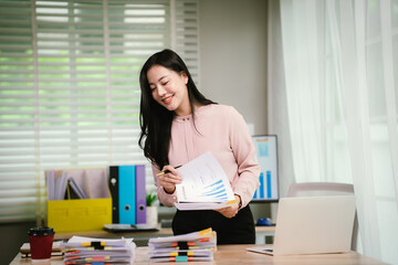 A cheerful businesswoman organizes stacks of documents at her desk, surrounded by charts, folders,...