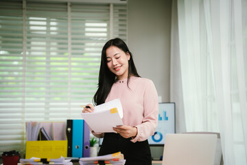 A cheerful businesswoman organizes stacks of documents at her desk, surrounded by charts, folders,...