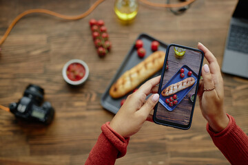 Hands of woman holding smartphone photographing freshly baked baguette and cherry tomatoes on...