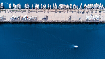 Aerial view of a long pier lined with boats contrasting with the deep blue sea, a lone boat cruising leaving a trail, Split, Split-Dalmatia County, Croatia.