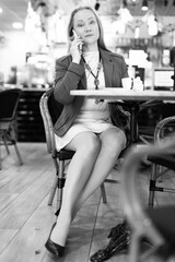 Woman sitting at table of cafe, drinking coffee and having telephone conversation