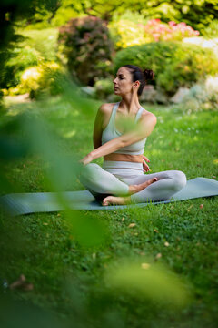Attractive woman wearing sports clothes and doing yoga in the garden at home