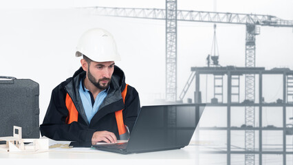 Construction engineer in safety gear working on a laptop with building site and cranes in background, analyzing project plans. Architecture, construction, civil engineering.