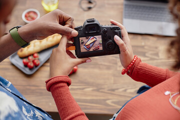 Young adult Black man and young adult woman photographing food with digital camera, hands holding...