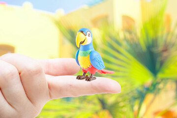 Close-up of a toy parrot on a finger. A very small domestic bird.