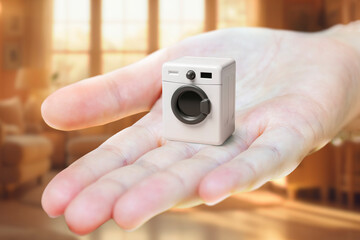 A toy washing machine on an outstretched palm. The concept of compact household appliances for a small apartment.