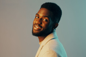 Obraz premium A cheerful Black man in a stylish light sweater smiles confidently against a soft gradient background, embodying warmth and creativity in a modern portrait