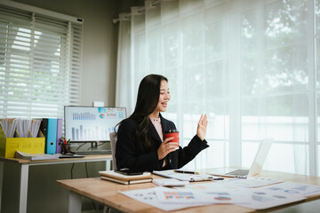 A focused businesswoman works at her desk, analyzing charts and graphs on a monitor, surrounded by documents, showing productivity, strategy, and success in a modern office environment.