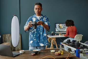 Young adult Black man adjusting digital camera in food photography studio, preparing to photograph...