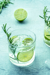 Gin tonic, a cocktail of gin with soda, lime, rosemary, and plenty of ice, on a blue background, fresh summer drink