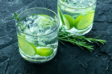 Gin tonic, two glasses of gin with soda, lime, rosemary, and ice, on a dark background, fresh summer drinks