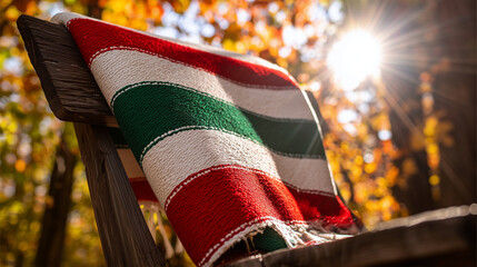 A traditional embroidered serape poncho in bold stripes of red, green, and white, draped over a rustic wooden chair with soft sunlight.