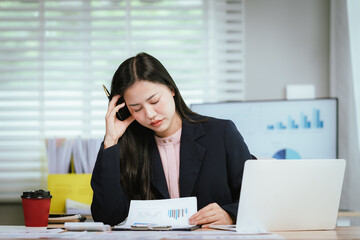 A tired businesswoman sits at her desk, visibly stressed and overworked, struggling with burnout,...