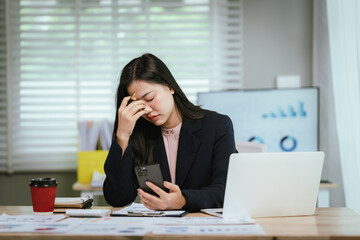 A tired businesswoman sits at her desk, visibly stressed and overworked, struggling with burnout,...