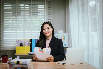 A professional woman sits at a bright, modern office desk, smiling while efficiently sorting...