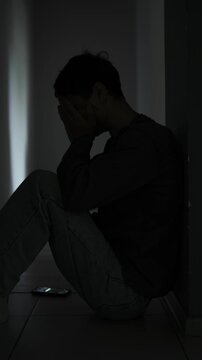 Broken hearted man sitting alone in dark room after breakup. Vertical video