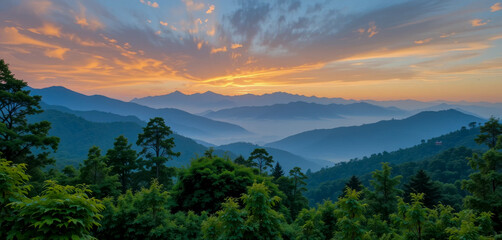 A breathtaking sunrise paints the sky with vibrant oranges and yellows, casting a warm glow over layers of misty mountains and lush green forests.