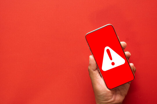 A mobile security warning concept. A smartphone screen shows a red alert, symbolizing a cybersecurity threat such as a virus, malware infection, or a hacking attempt.red background with copyspace.
