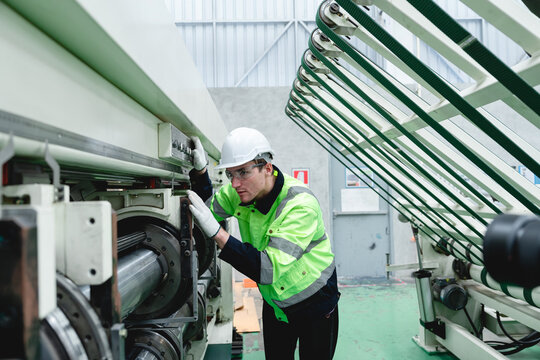 Engineer at cardboard plant performs quality control check on industrial equipment, emphasizing safety protocols and smooth operation of production systems.
