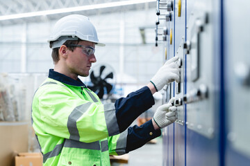 Caucasian male engineer in safety gear operates industrial machine using control panel in cardboard packaging factory, showing confidence, knowledge, and safety compliance.