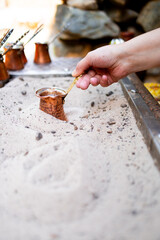 Preparing traditional Turkish coffee in sand with copper pot and hand