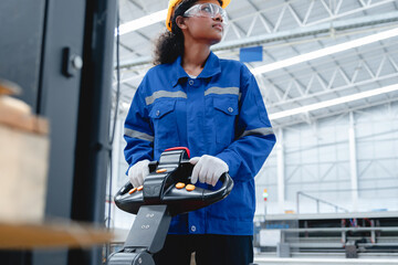 Black female factory worker in safety helmet and blue uniform operates electric forklift truck...