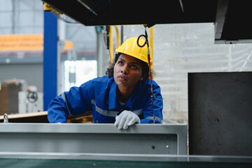 Inside a packaging factory, Southeast Asian worker inspects machinery operation with serious...