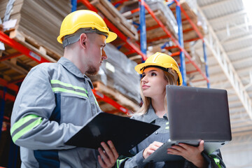 Professional logistics team checking cardboard supply data using digital tools and documents in storage facility with high stacked packaging boxes.