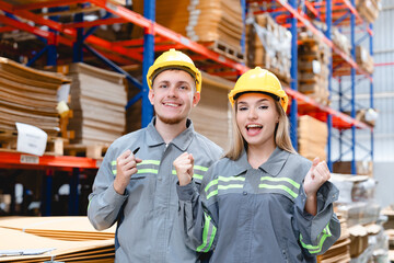 Happy warehouse staff wearing uniforms and hard hats celebrating teamwork achievement inside a cardboard packaging factory, showing unity and positive energy.

