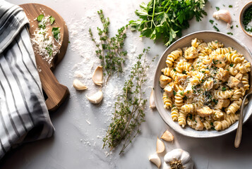 Creative food template. Creamy garlic parmesan rotini pasta with chicken cubes, freshly grated cheese shavings and parsley, scattered garlic cloves on messy counter top. copy text space. top flat lay 