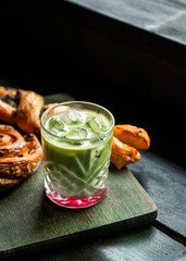 Refreshing strawberry matcha latte served with assorted pastries on a wooden board placed over a rustic table. Cozy and inviting cafe-style setup with natural lighting, perfect for brunch or an aftern