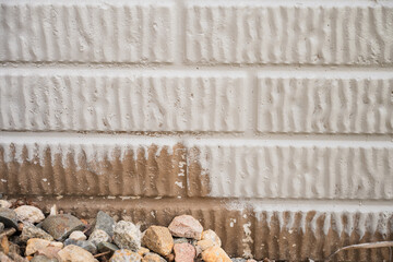 Painting block exterior wall with dirt stains and loose gravel near the foundation of a house