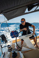 Man standing at the helm of a sailing yacht near Croatia, steering the boat through open water. Leadership, control, sailing lifestyle and freedom at sea.