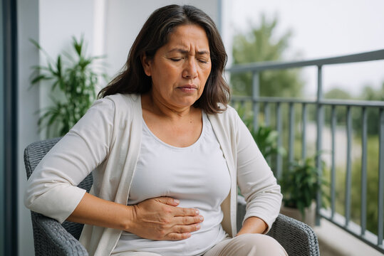 Middle-aged woman experiencing discomfort while seated on balcony with potted plants, reflecting emotional stress and health concerns in a peaceful outdoor setting