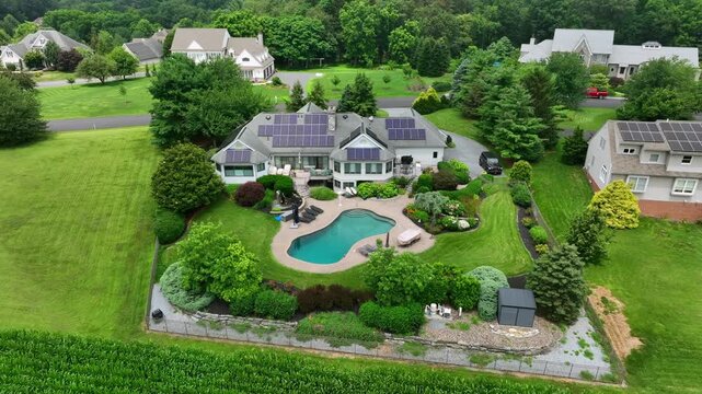Exclusive villa with solar panels on roof and swimming pool in garden.Aerial orbit shot. Luxurious American suburban estate in landscaped yard and kidney-shaped pool.Modern colonial-style architecture