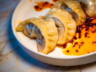 Close-up of a plate of pan-fried dumplings gyoza jiaozi , served with a generous amount of chili...