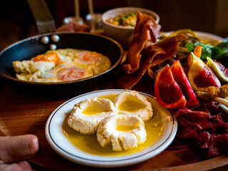Middle Eastern brunch platter spread. Fresh Cheese with Olive Oil. Fried Eggs in a Pan. Cured Meats and Prosciutto